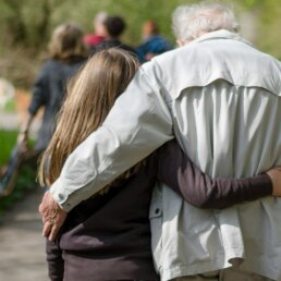 A grandparent and grandchild walking arm in arm along a tree-lined path, an autumn day out with elderly parents